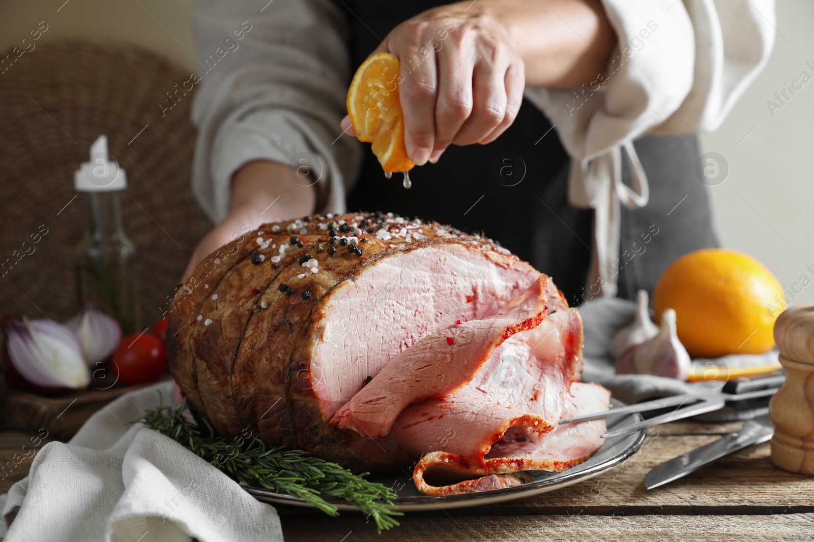 Photo of Woman squeezing juice from orange slice onto delicious baked ham at wooden table, closeup