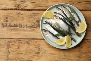 Photo of Fresh raw sprats, lemon and dill on wooden table, top view. Space for text