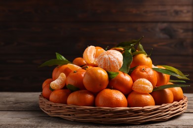 Photo of Fresh ripe juicy tangerines and green leaves on wooden table