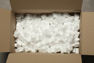 Photo of One open cardboard box with pieces of polystyrene foam on grey floor, top view