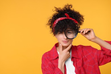Curious young woman looking through magnifier glass on yellow background. Space for text