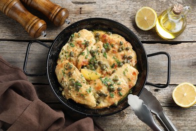 Delicious chicken piccata with herbs and lemon on wooden table, flat lay