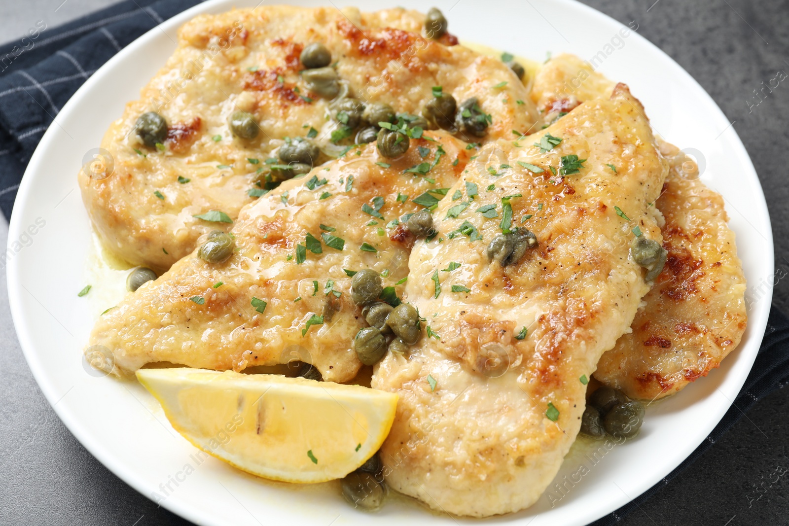 Photo of Delicious chicken piccata with herbs on grey table