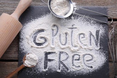 Photo of Kitchen utensils and phrase Gluten free written with flour on wooden table, flat lay