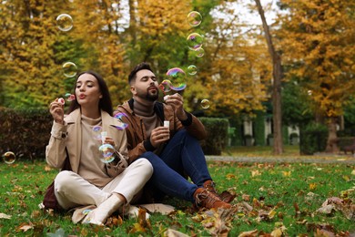 Photo of Happy young couple blowing soap bubbles in autumn park, space for text