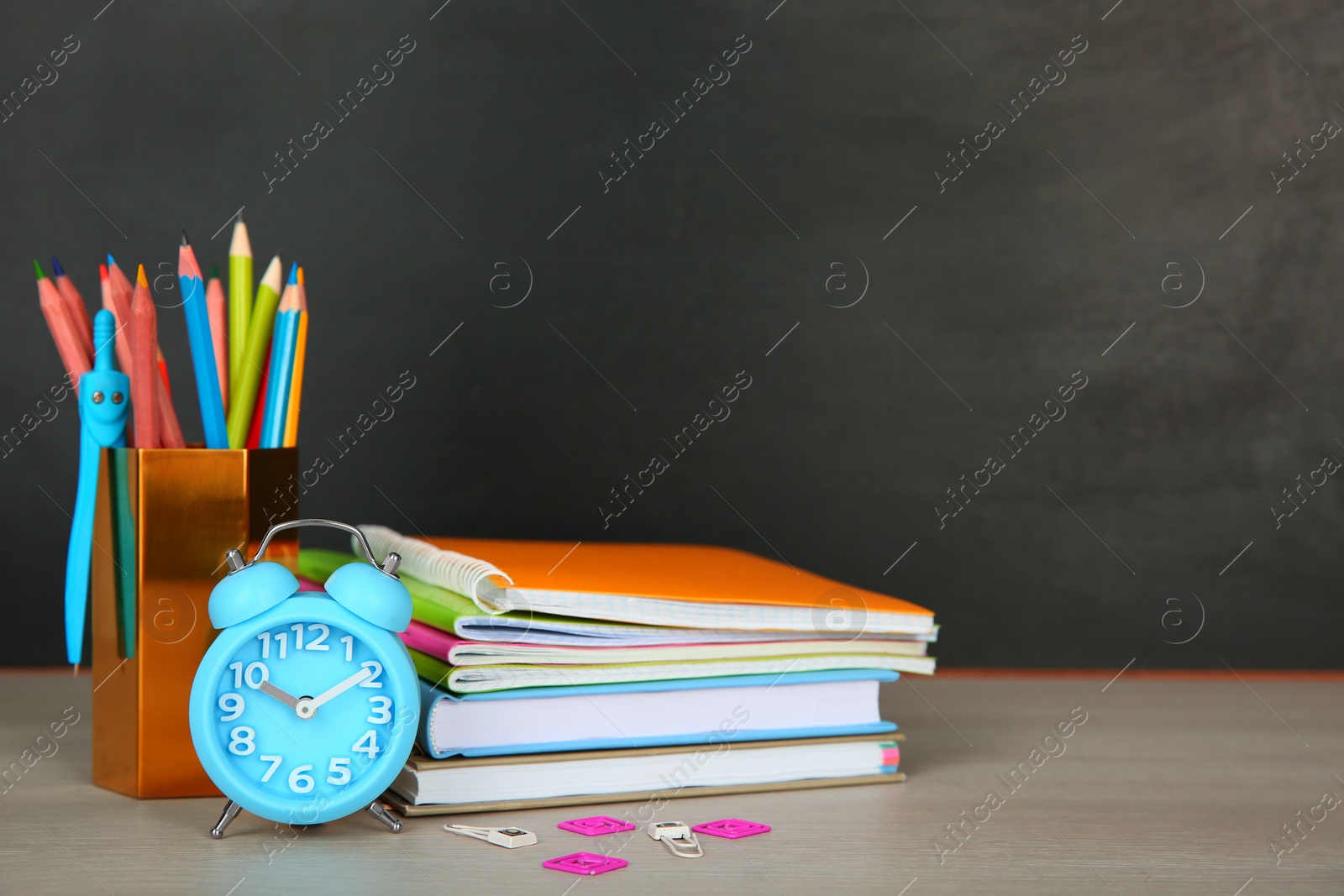 Photo of Composition with stationery and alarm clock on table near blackboard, space for text. Doing homework