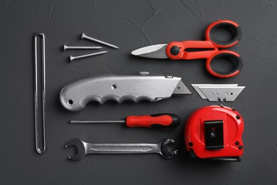 Photo of Utility knife with blades among other tools on dark grey background, flat lay