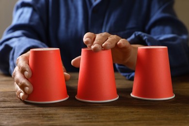 Woman playing thimblerig game with red cups at wooden table, closeup