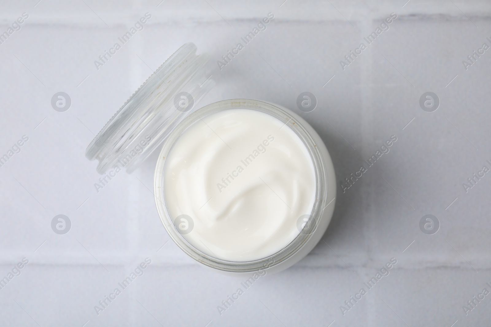 Photo of Delicious natural yogurt in glass jar on white tiled table, top view