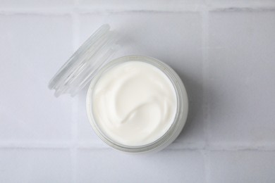 Delicious natural yogurt in glass jar on white tiled table, top view