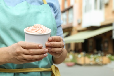 Photo of Woman holding cup with tasty frozen yogurt outdoors, closeup. Space for text