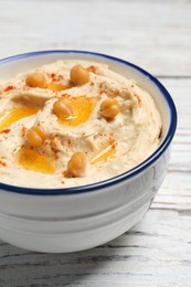 Photo of Bowl of tasty hummus with chickpeas and paprika on white wooden table, closeup