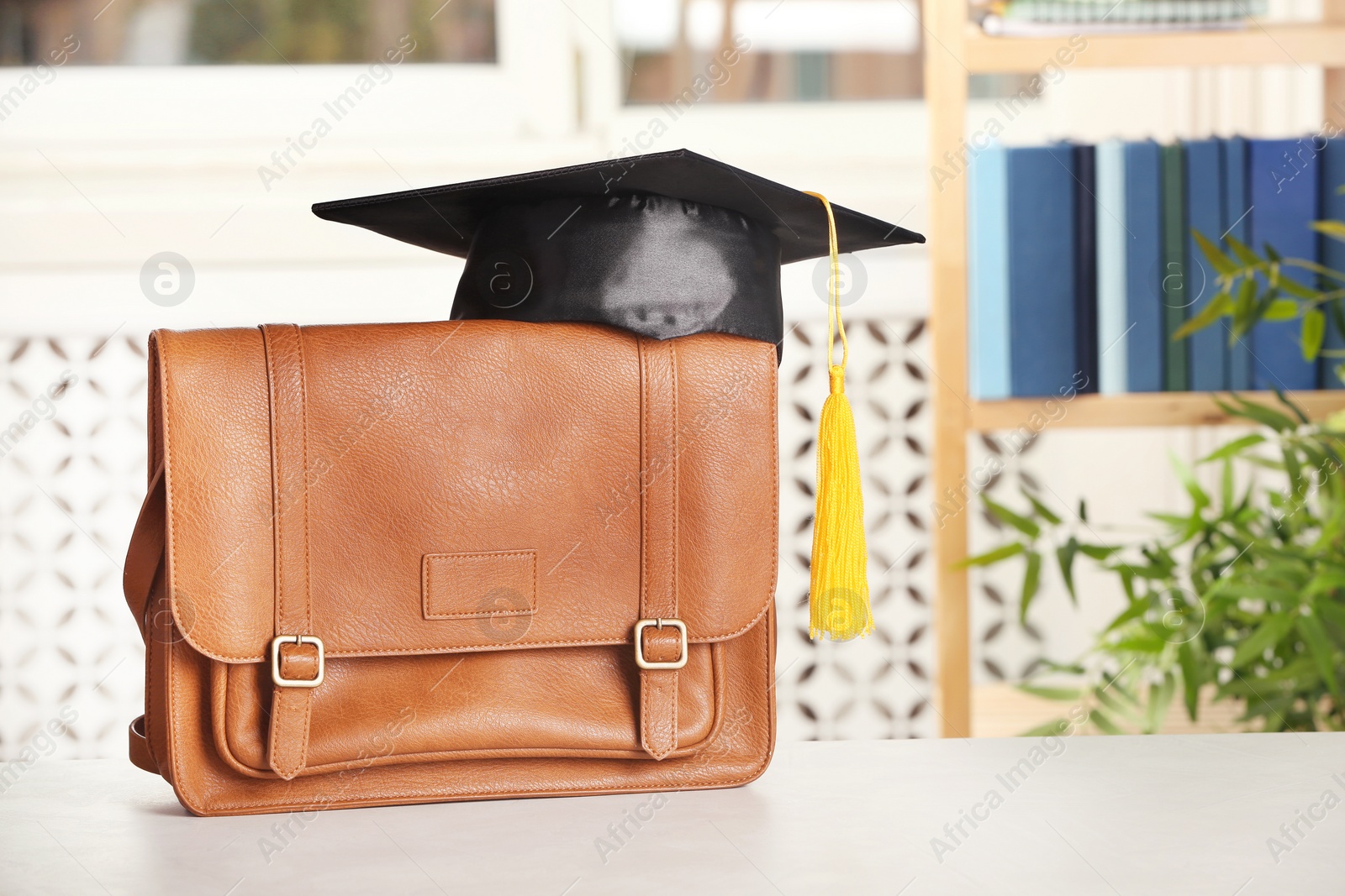 Photo of Briefcase with graduation hat on table against blurred background