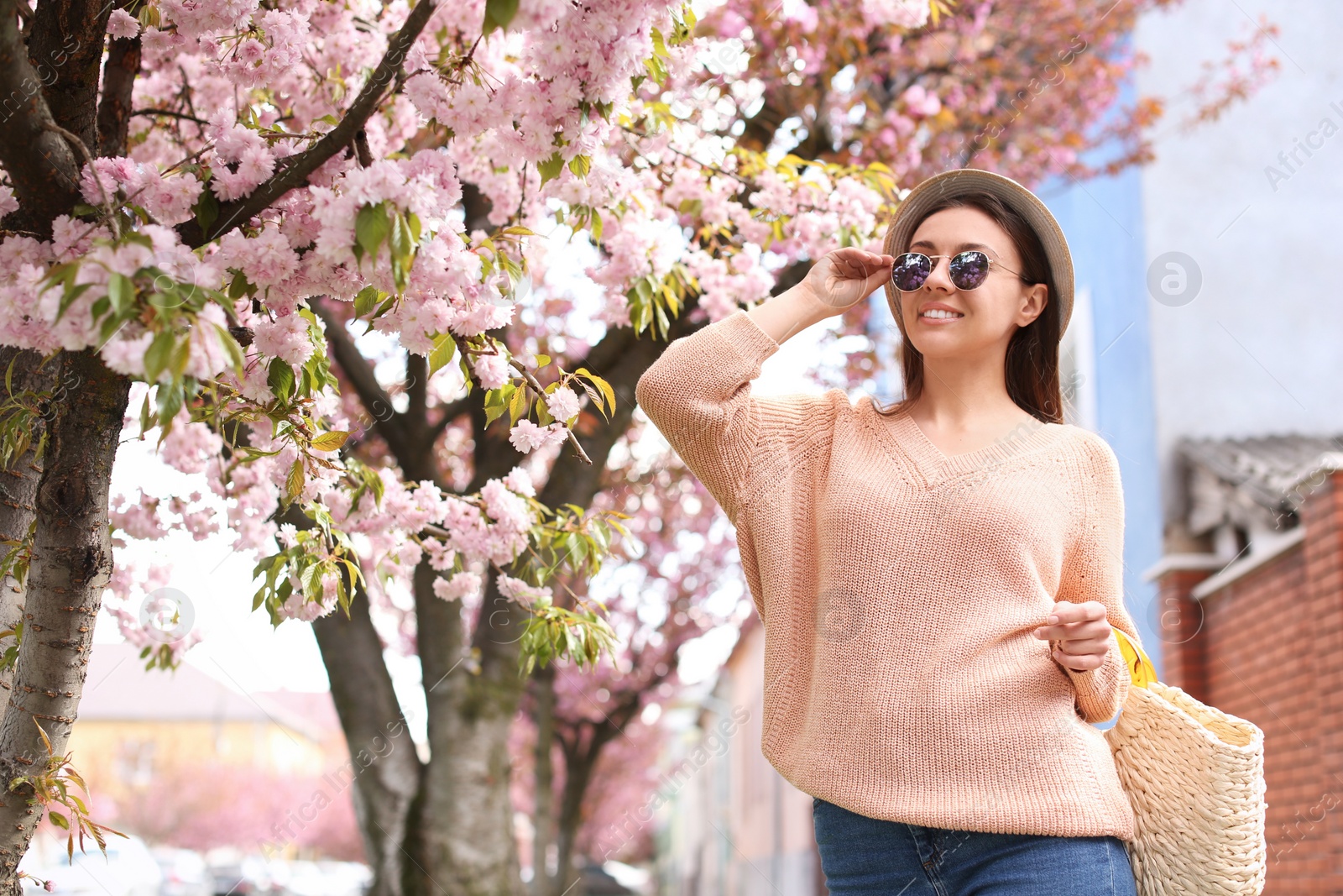 Photo of Happy stylish young woman near blossoming sakura tree outdoors. Spring look