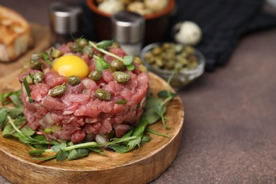 Photo of Tasty beef steak tartare served with yolk, capers and microgreens on brown table, closeup. Space for text