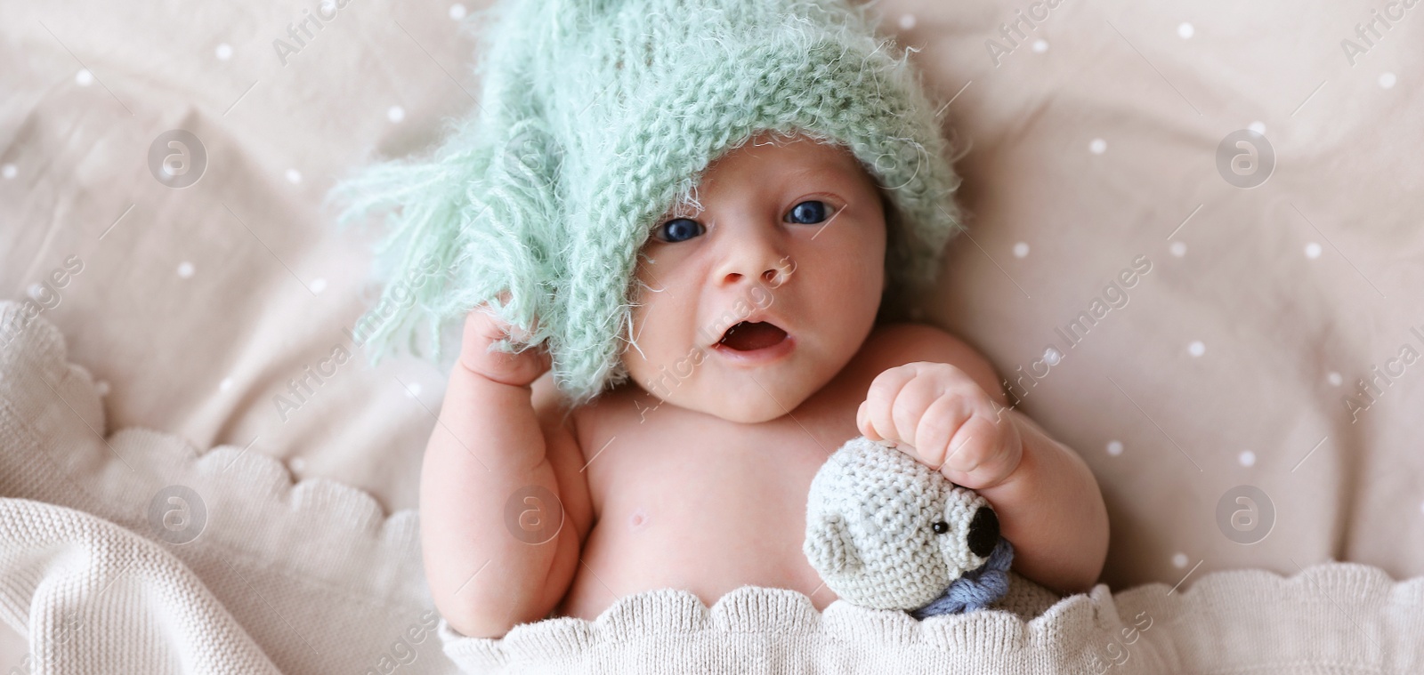 Image of Cute newborn baby in warm hat with toy lying on bed, top view. Banner design