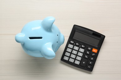 Photo of Calculator and piggy bank on white wooden table, top view