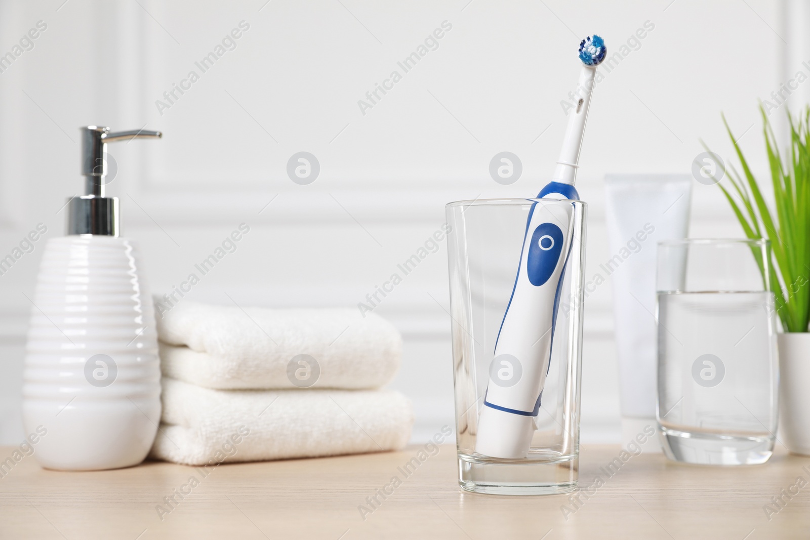 Photo of Electric toothbrush, glass of water and toiletries on wooden table