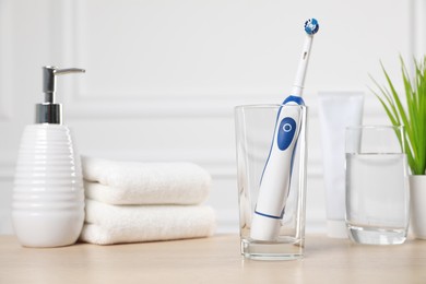 Electric toothbrush, glass of water and toiletries on wooden table