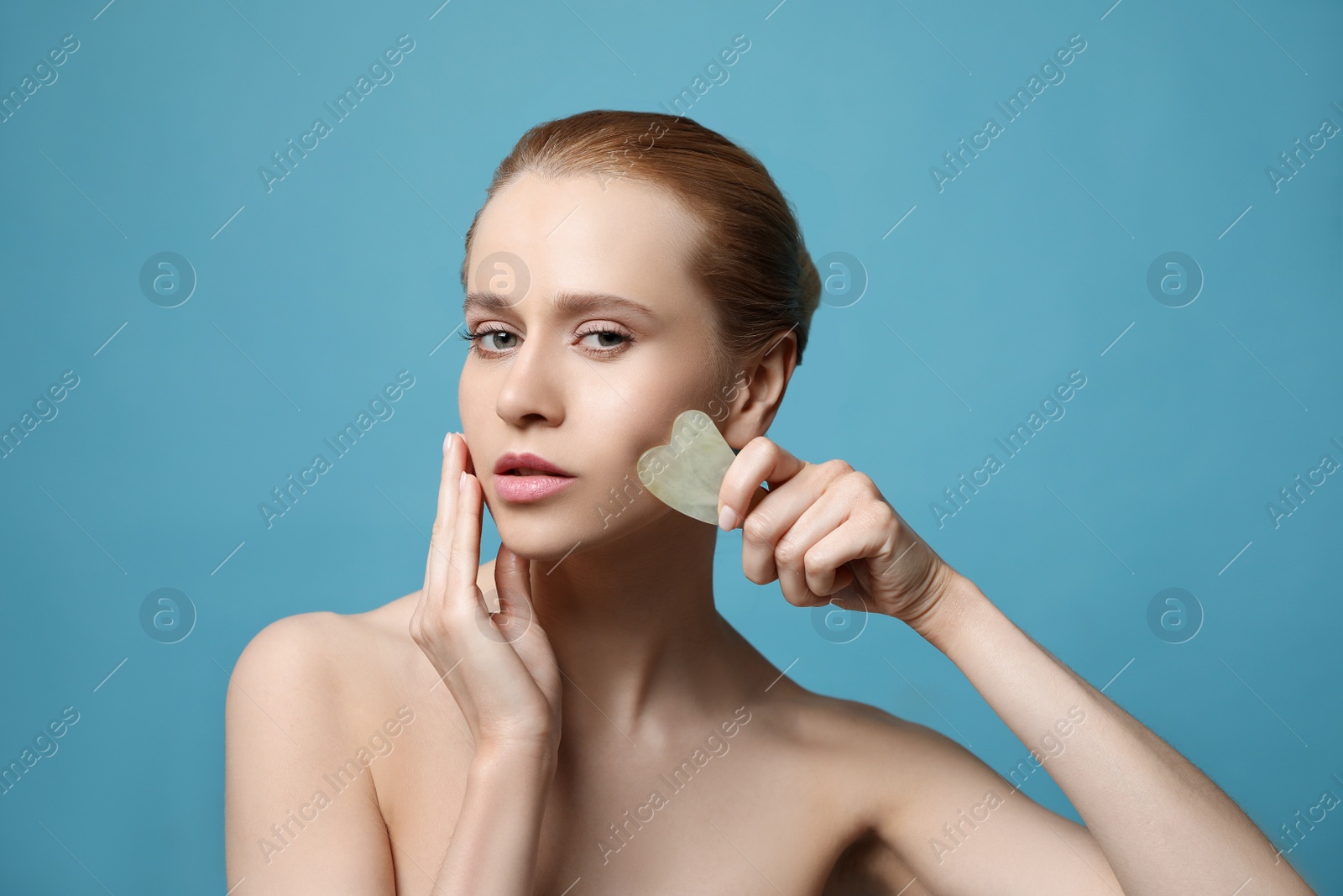 Photo of Beautiful young woman doing facial massage with gua sha tool on blue background