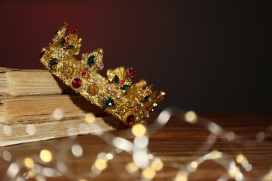 Beautiful golden crown, old books and fairy lights on brown background. Fantasy item