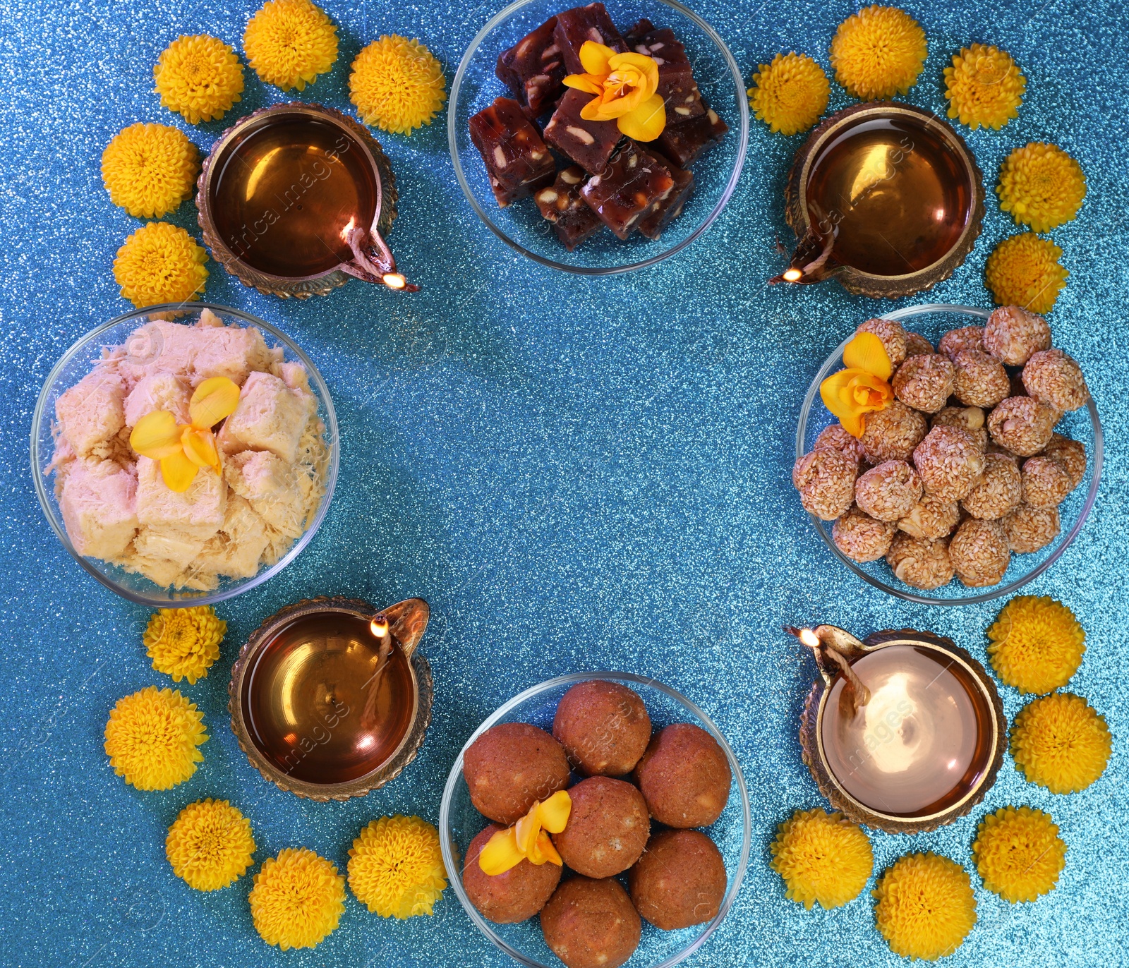 Photo of Diwali celebration. Frame made of diya lamps, tasty Indian sweets and chrysanthemum flowers on shiny light blue table, flat lay with space for text