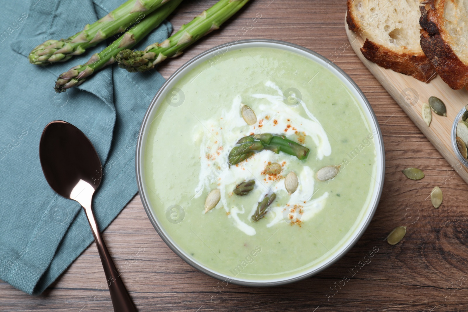 Photo of Delicious asparagus soup with pumpkin seeds served on wooden table, flat lay