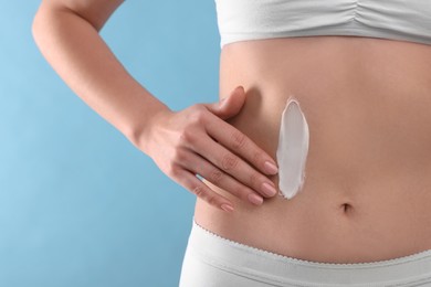 Photo of Woman with smear of body cream on her belly against light blue background, closeup