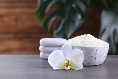 Photo of Natural sea salt in bowl, spa stones and beautiful orchid flower on wooden table. Space for text