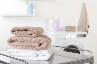 Photo of Stack of clean soft towels on table in laundry room. Space for text
