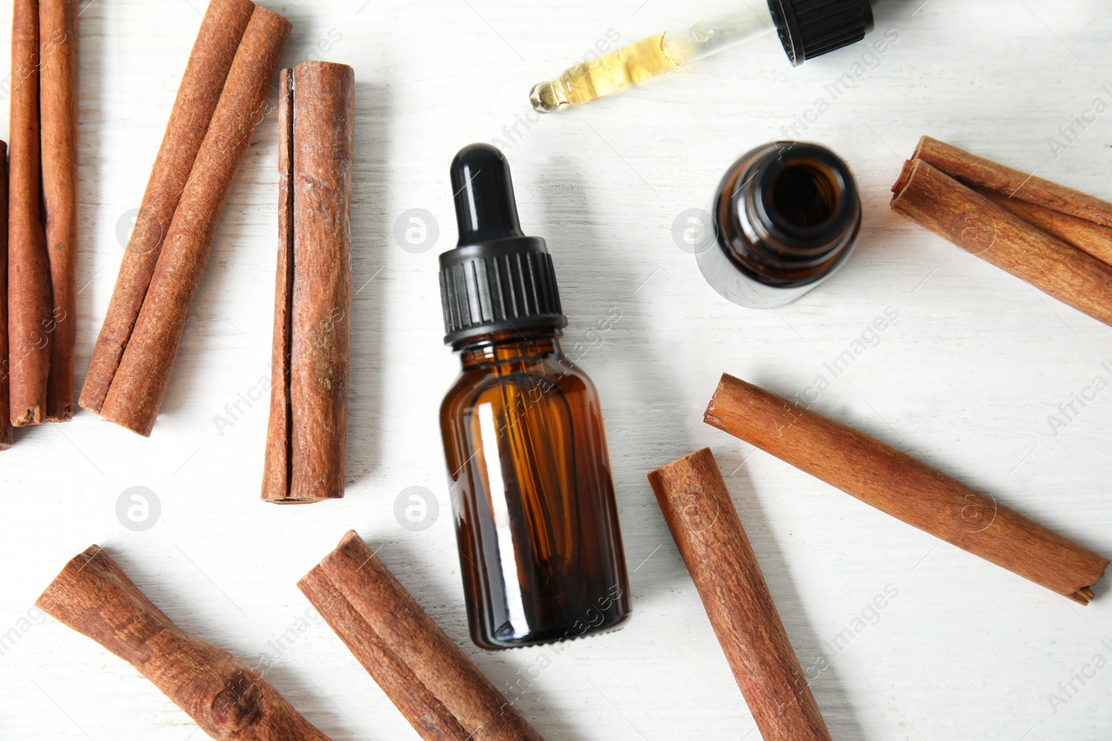 Photo of Bottles of essential oils and cinnamon sticks on white wooden table, flat lay