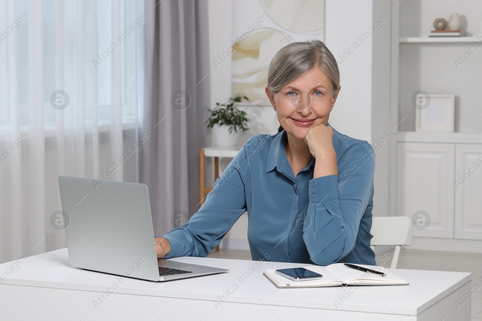 Photo of Beautiful senior woman near laptop at white table indoors