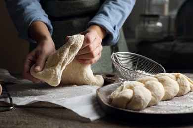Woman making braided bread at wooden table indoors, closeup. Traditional Shabbat challah