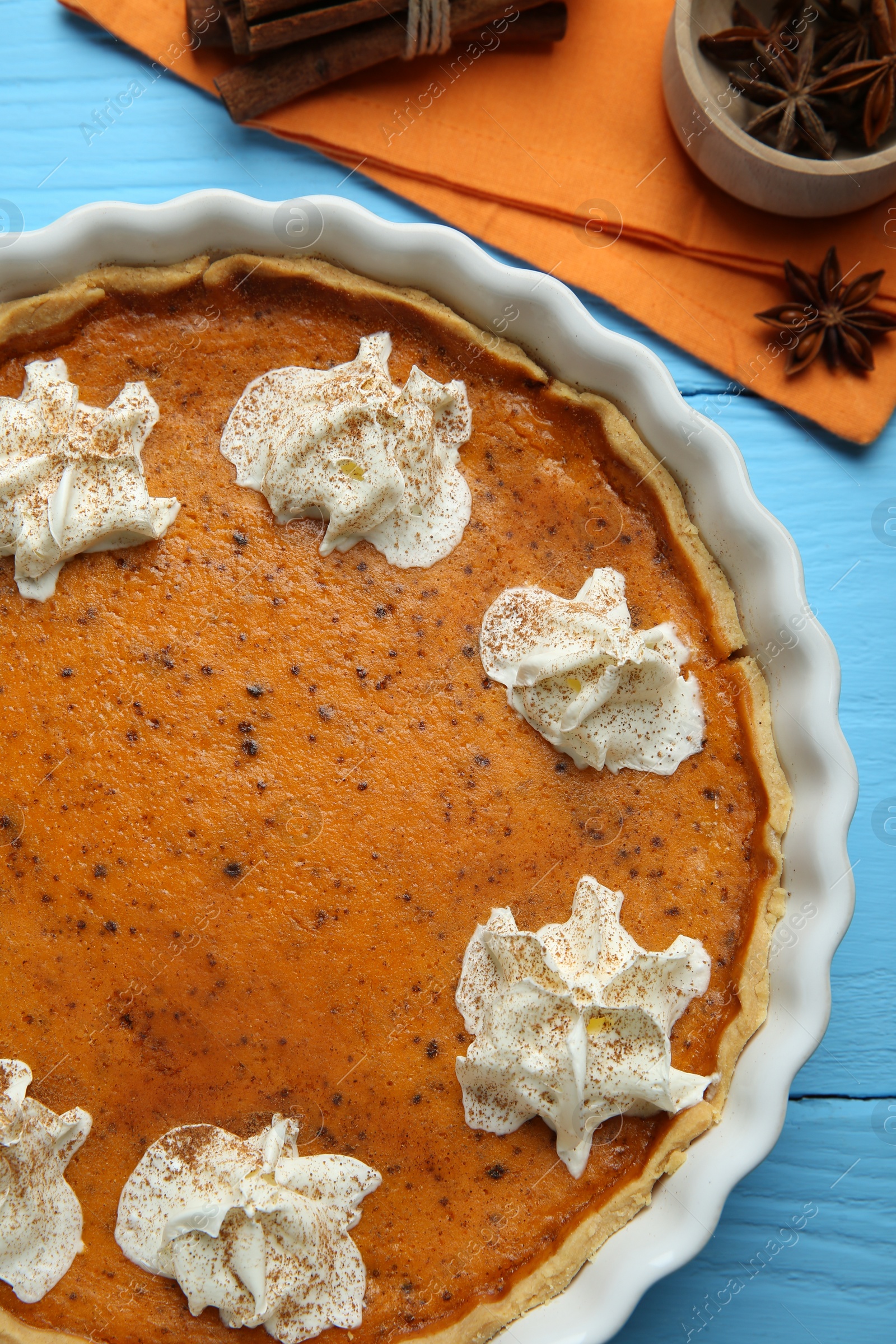 Photo of Delicious pumpkin pie with whipped cream and spices on light blue wooden table, top view