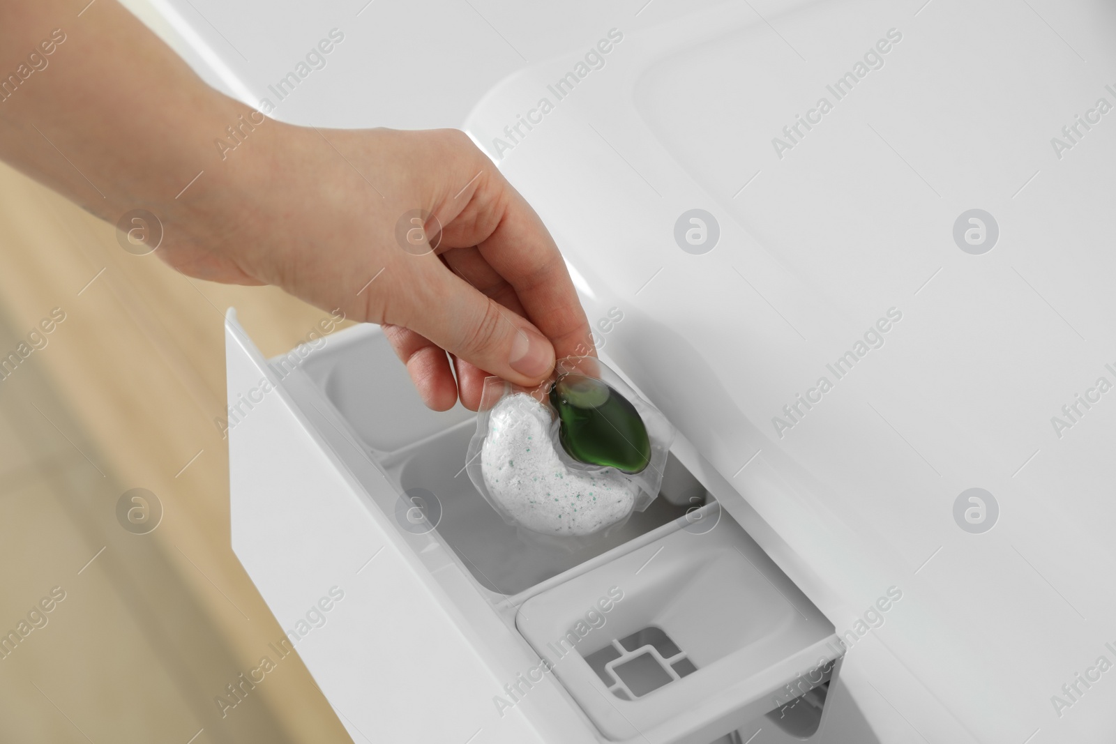 Photo of Woman putting laundry detergent capsule into washing machine, closeup