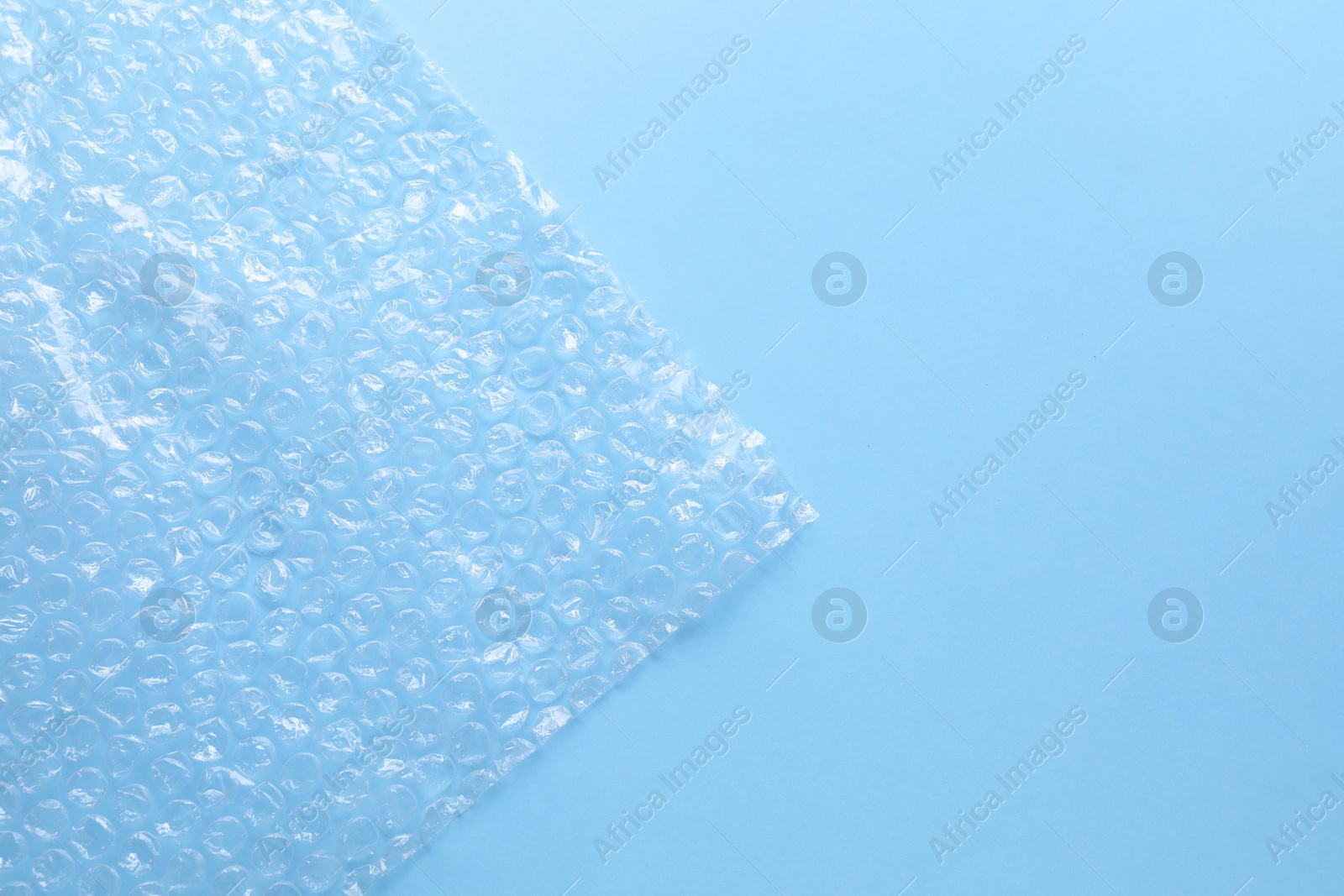 Photo of Transparent bubble wrap on light blue background, top view. Space for text