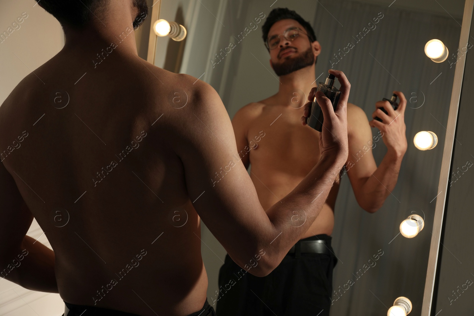 Photo of Man spraying luxury perfume near mirror indoors