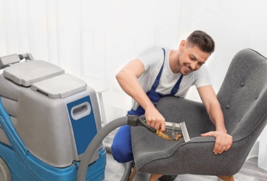 Photo of Dry cleaning worker removing dirt from armchair indoors