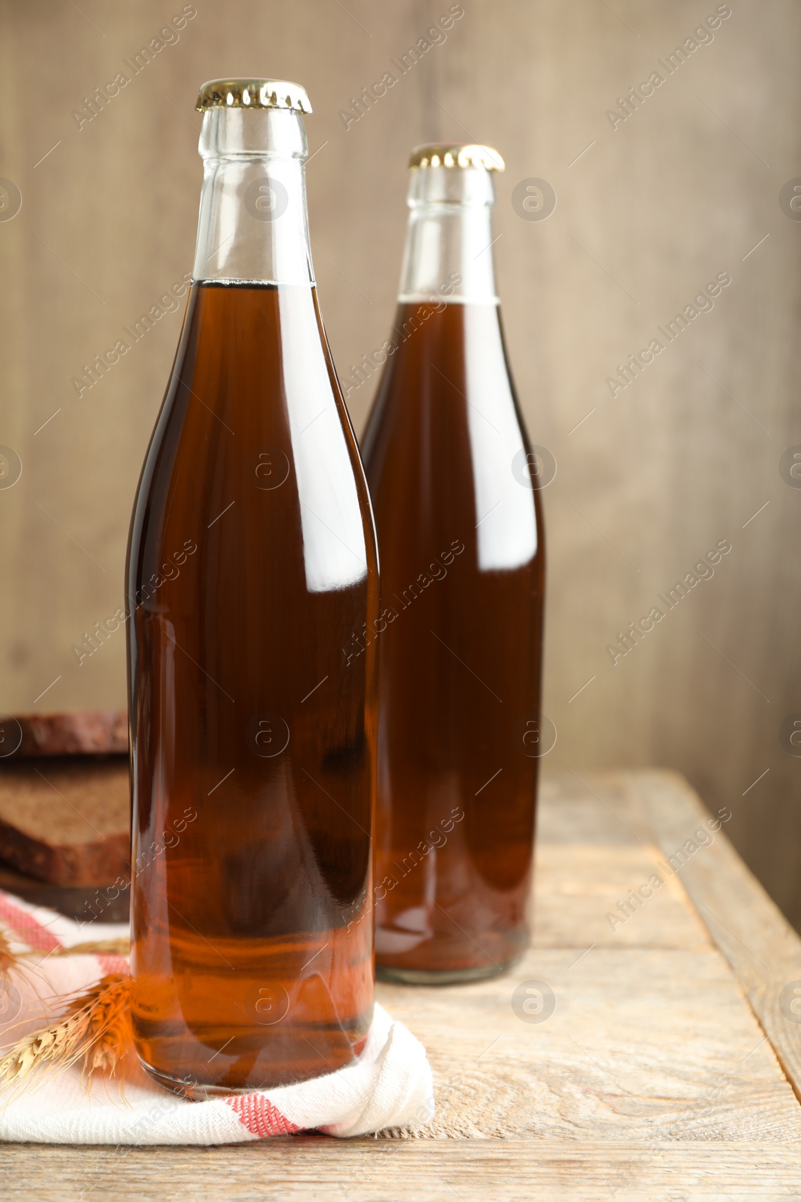 Photo of Bottles of delicious fresh kvass, spikelets and bread on wooden table