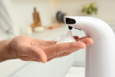 Man using automatic soap dispenser in kitchen, closeup