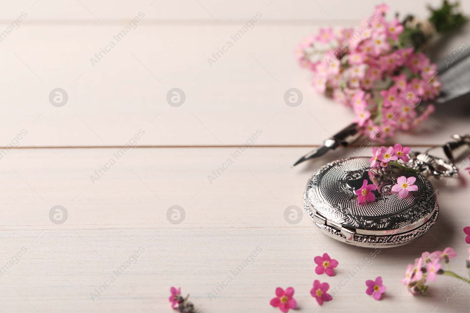 Photo of Beautiful Forget-me-not flowers, pocket watch and feather pen on white wooden table. Space for text