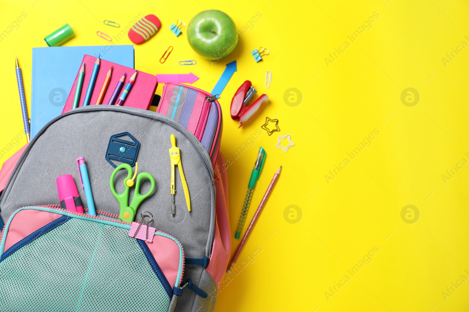 Photo of Stylish backpack with different school stationery on yellow background, flat lay