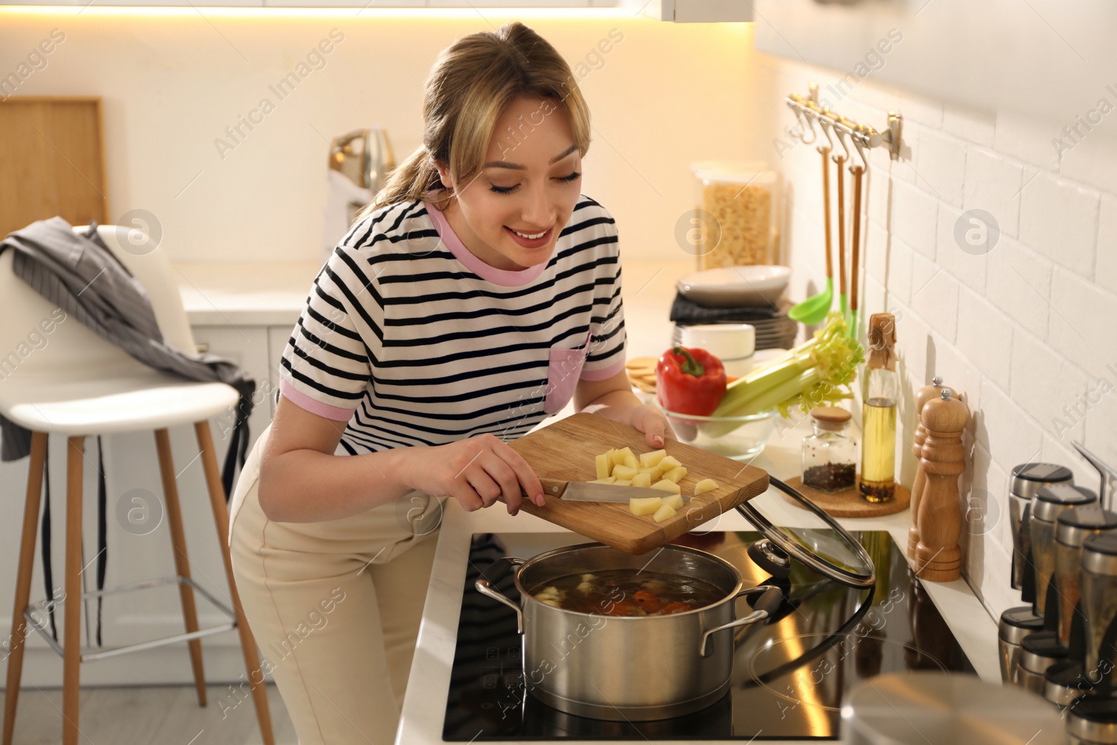 Photo of Woman putting potato into pot to make bouillon in kitchen. Homemade recipe