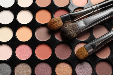 Photo of Beautiful eye shadow palette with brushes as background, top view