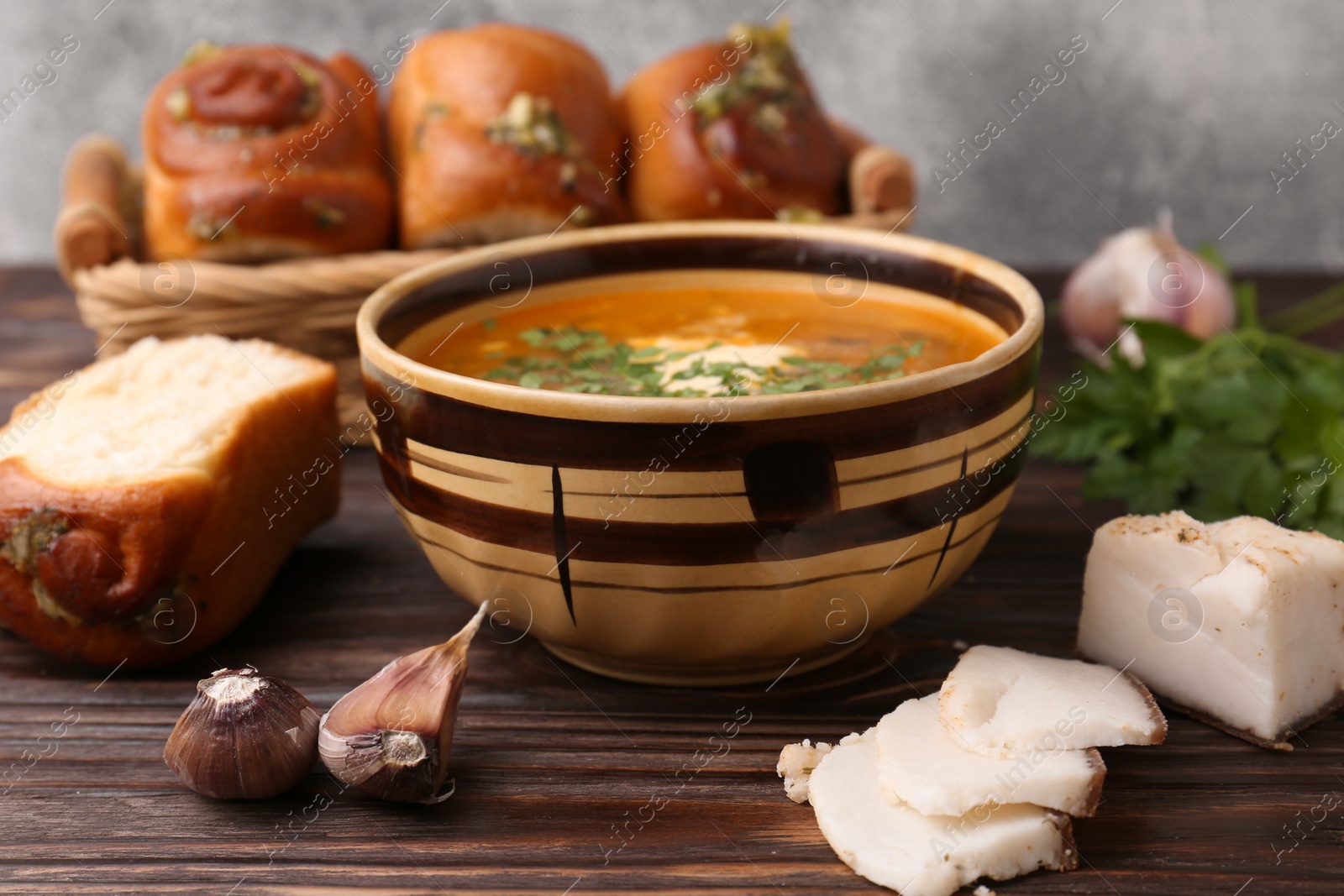 Photo of Delicious borsch served with pampushky and salo on wooden table, closeup. Traditional Ukrainian cuisine