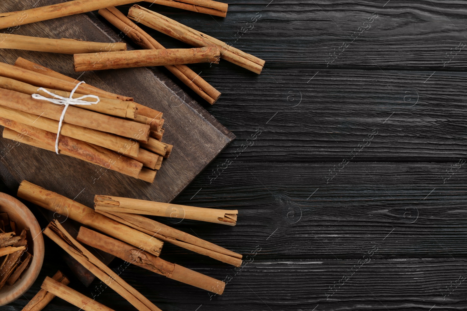 Photo of Aromatic cinnamon sticks on black wooden table, flat lay. Space for text