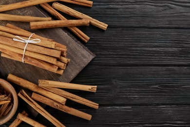 Photo of Aromatic cinnamon sticks on black wooden table, flat lay. Space for text