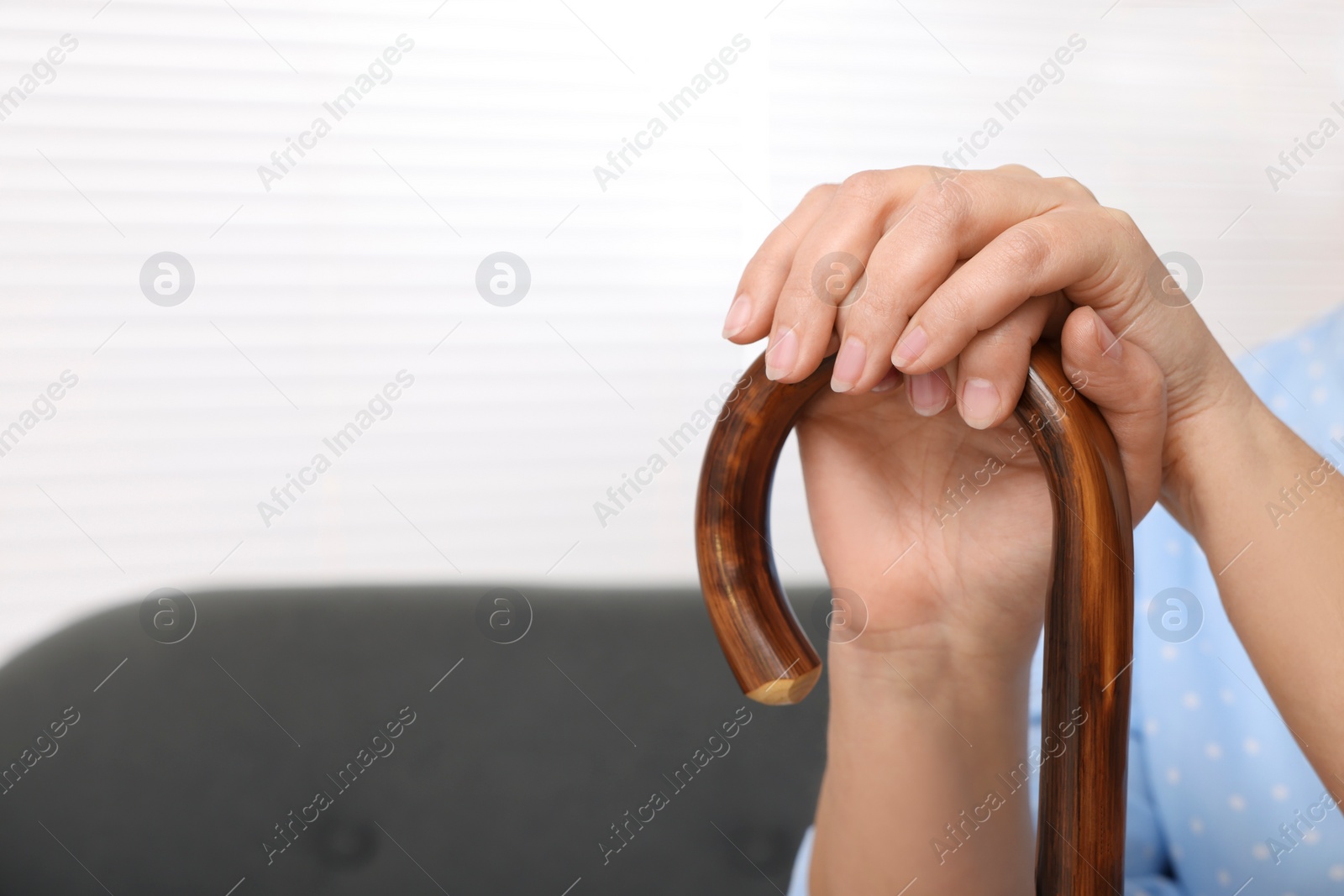 Photo of Senior woman with walking cane sitting on sofa at home, closeup. Space for text