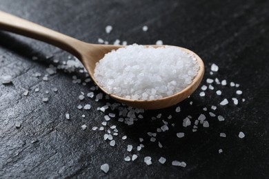 Photo of Organic white salt and spoon on black table, closeup