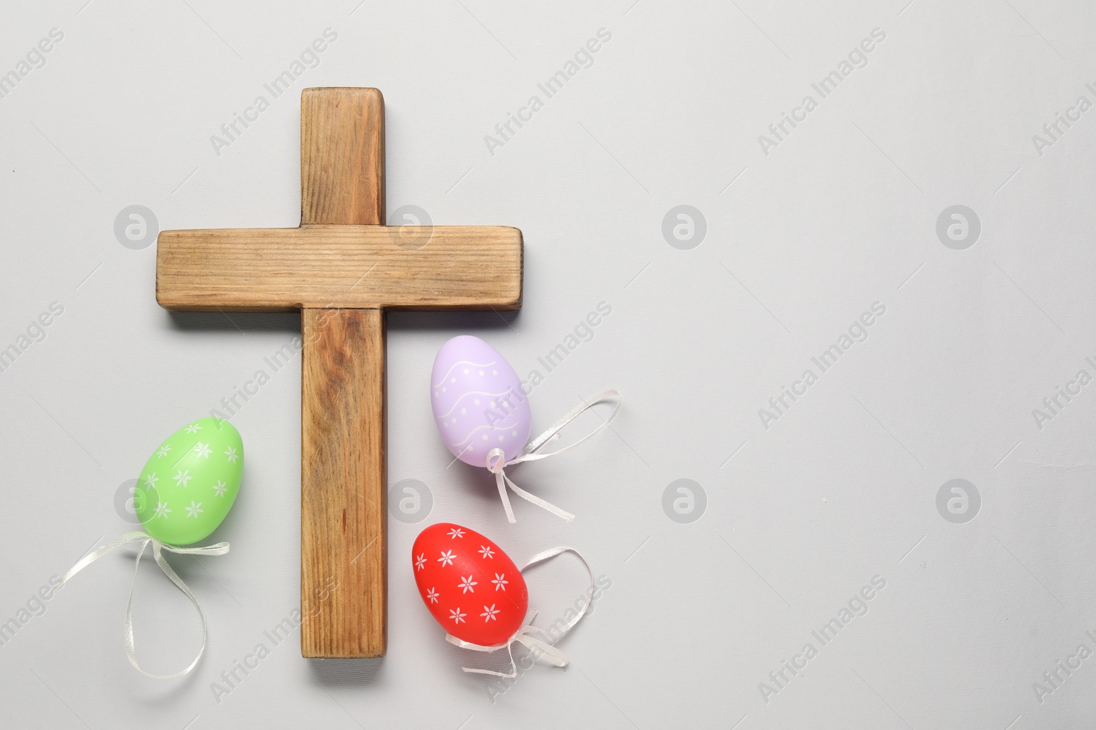 Photo of Wooden cross and painted Easter eggs on light grey background, flat lay. Space for text